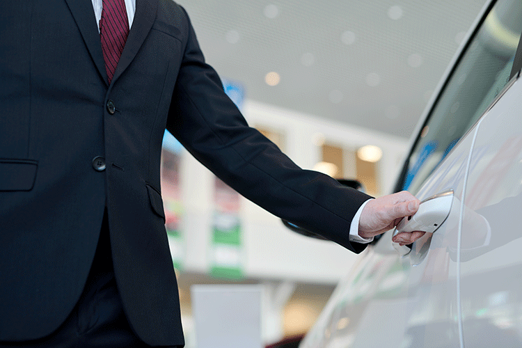 A professional chauffeur in a suit and red tie opening the door of a white luxury car, representing the premium chauffeured car rental service in Istanbul.