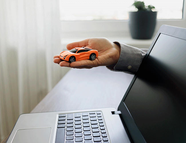 A hand holding a toy car over a laptop, symbolizing the ease of booking a luxury vehicle online with Limousine Plus in Istanbul.
