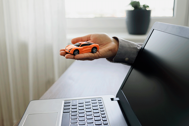 A hand holding a toy car over a laptop, symbolizing the ease of booking a luxury vehicle online with Limousine Plus in Istanbul.